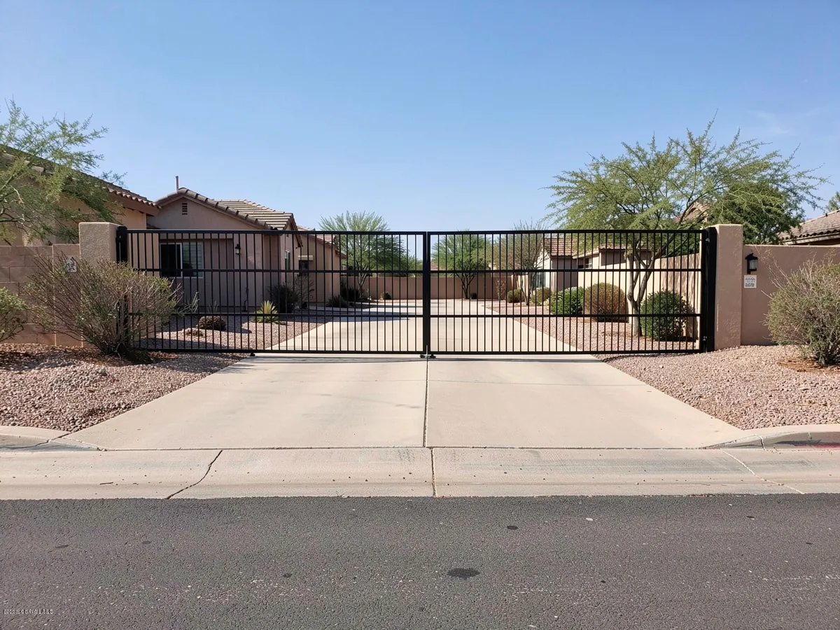 Wide black steel driveway gate set back from the street behind a concrete apron